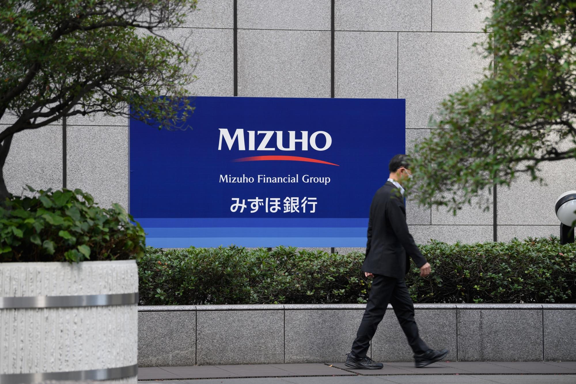 Pedestrian walking infront of Mizuho signage. PHOTO: Shutterstock